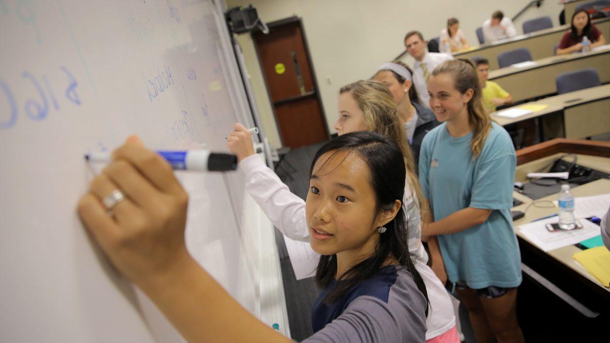 Students writing on a whiteboard.